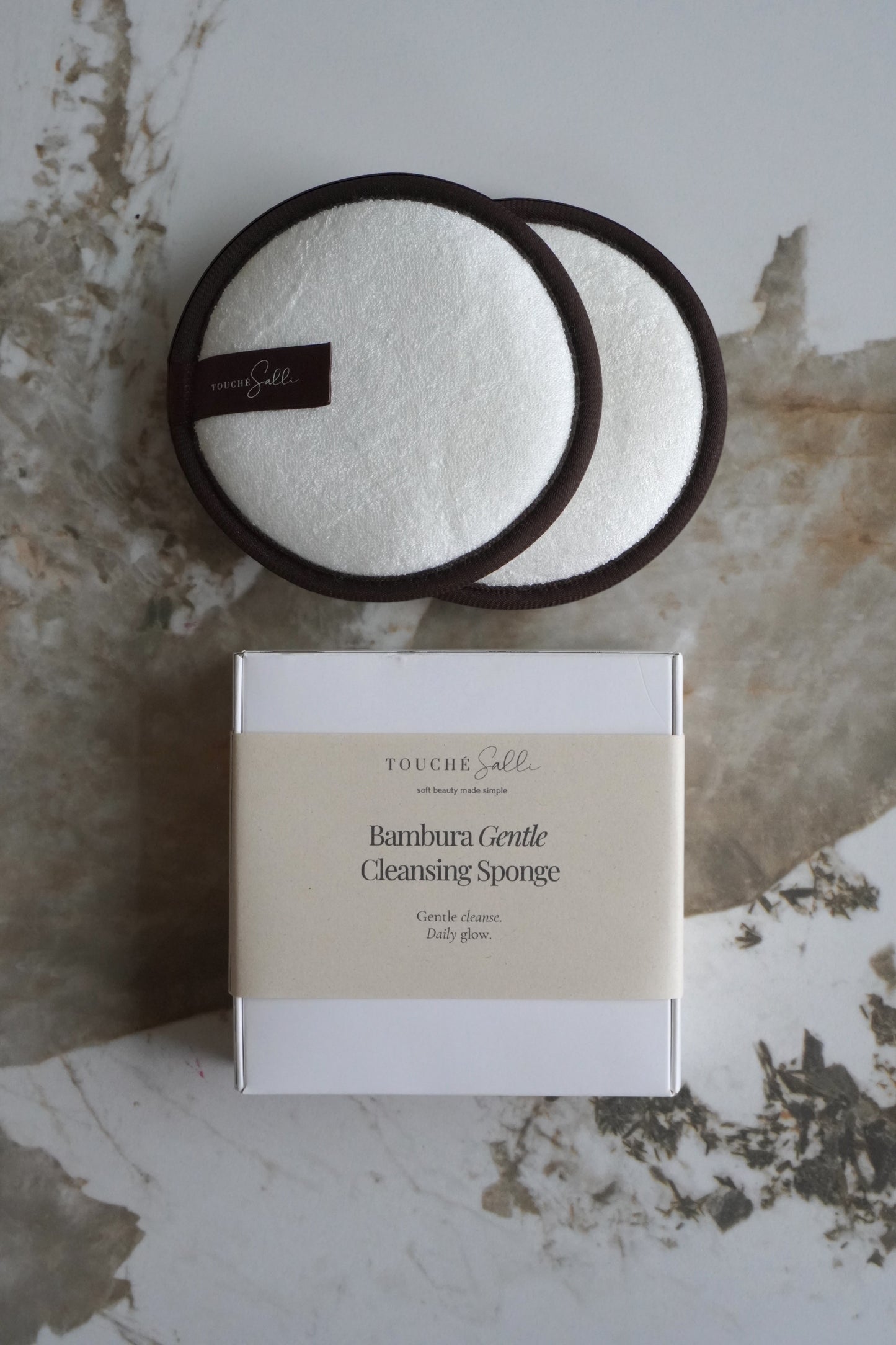 Touché Salli Bambura Gentle Cleansing Sponge, 2 stk. Hvide bambusfrotté svampe med mørkebrune kanter.